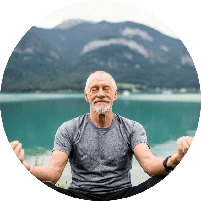 Elderly man meditating in front of a mountain lake