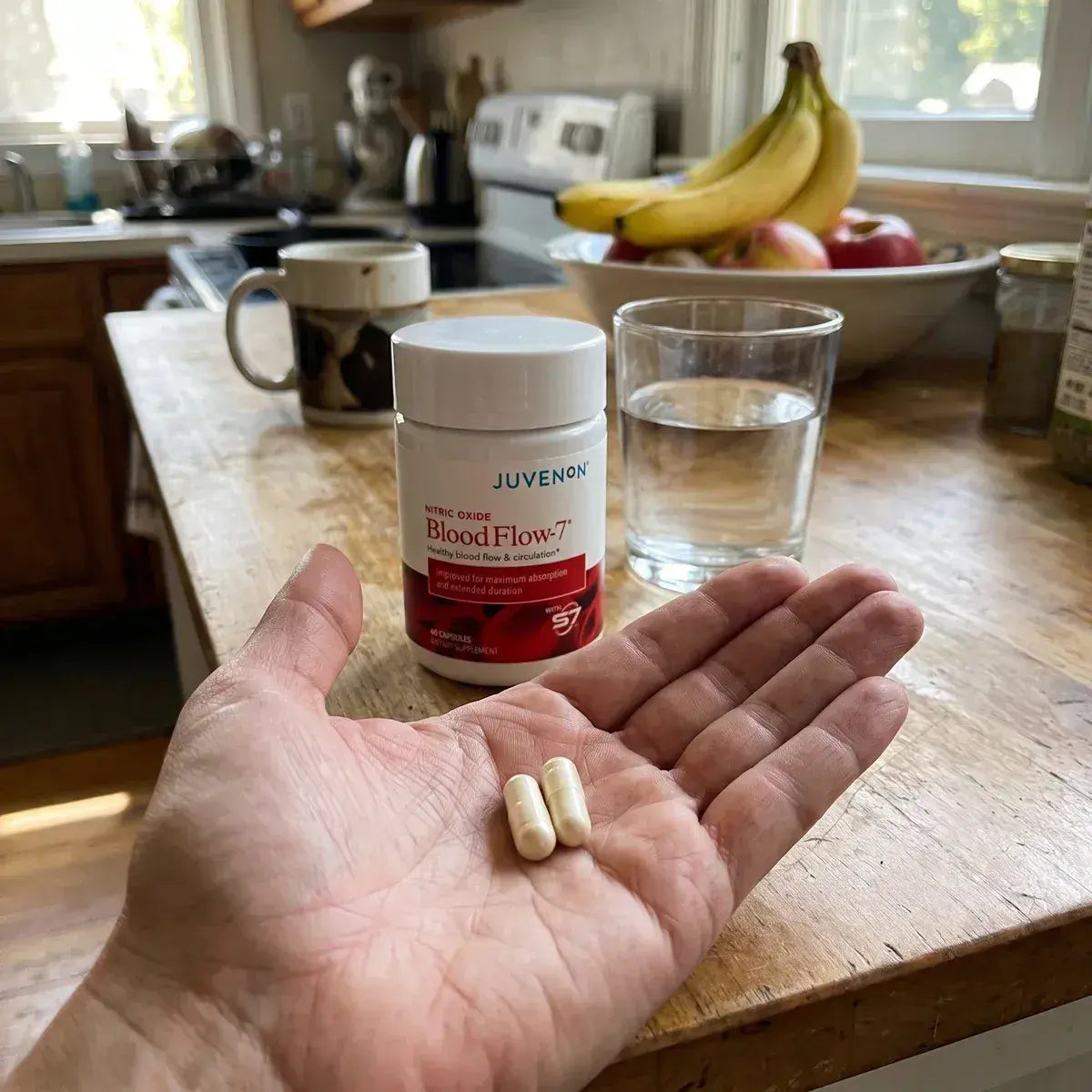 Two BloodFlow-7® capsules in a hand next to the bottle and a glass of water